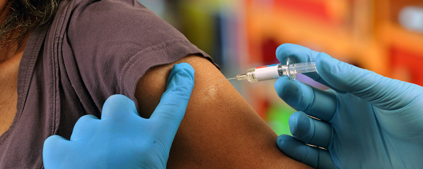 A healthcare professional administering a flu jab to a patient's arm. The needle is visible. The image illustrates the process of receiving a flu vaccination to prevent influenza.