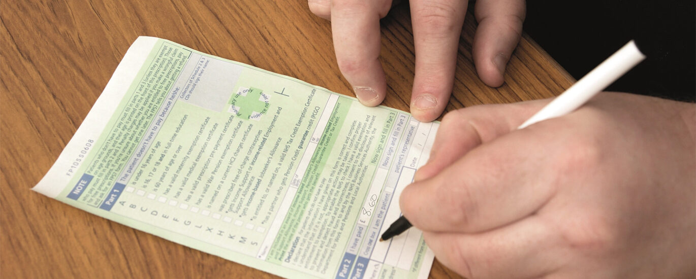 A patient signing the back of a green FP10 prescription before handing it to the pharmacist for clinical check and dispensing. This is different to the emergency prescriptions service offered at North Harrow Pharmacy.