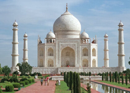 A stunning white marble mausoleum, the Taj Mahal in India, standing tall against a blue sky with intricate architectural details and reflecting in a serene pool of water. Travellers may visit this location after having their vaccinations.